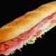 Long sub sandwich with layers of ham, salami, lettuce, tomatoes, and cheese on a crusty baguette